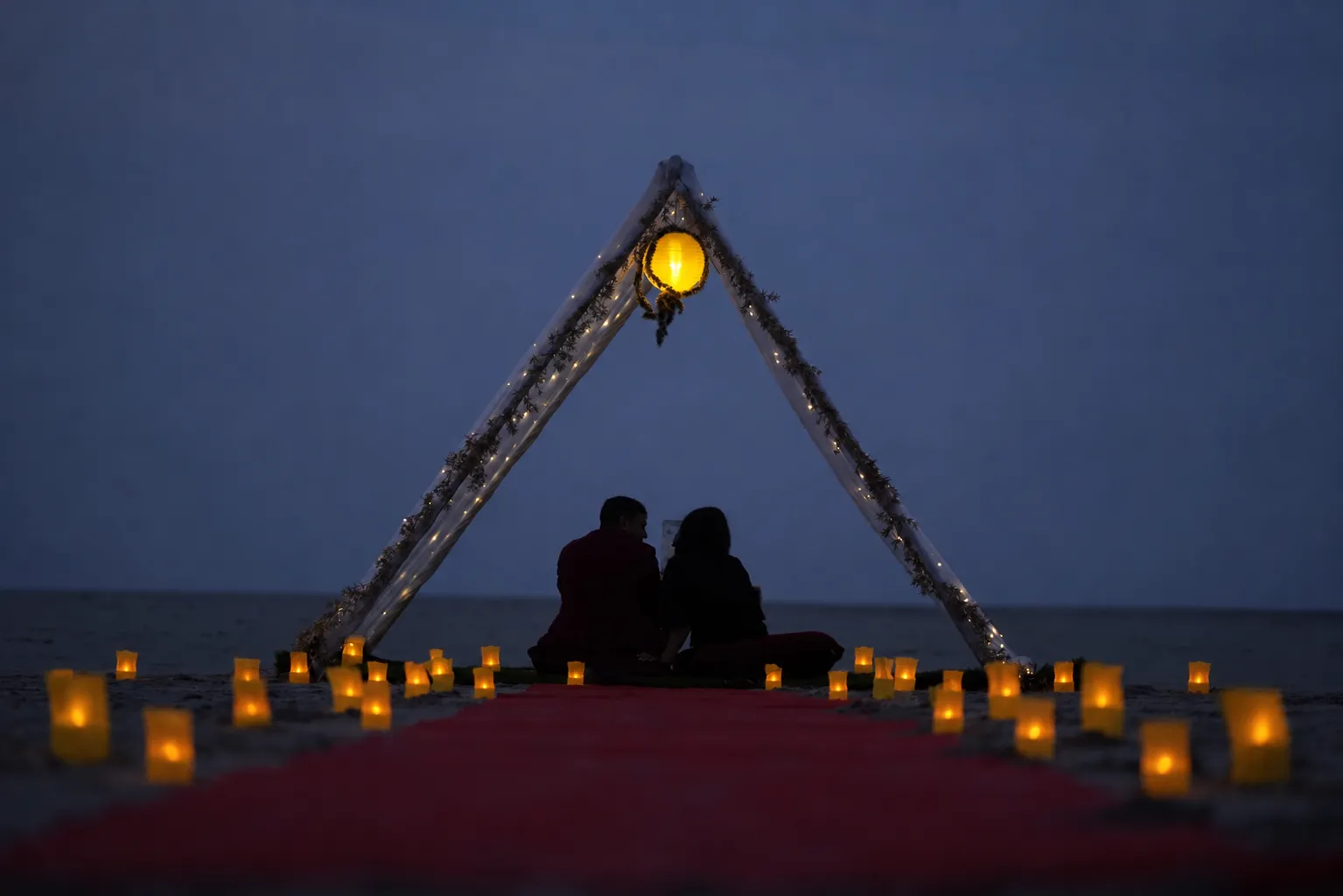 Couple at a candlelit island dinner beneath a lantern-lit arch at dusk