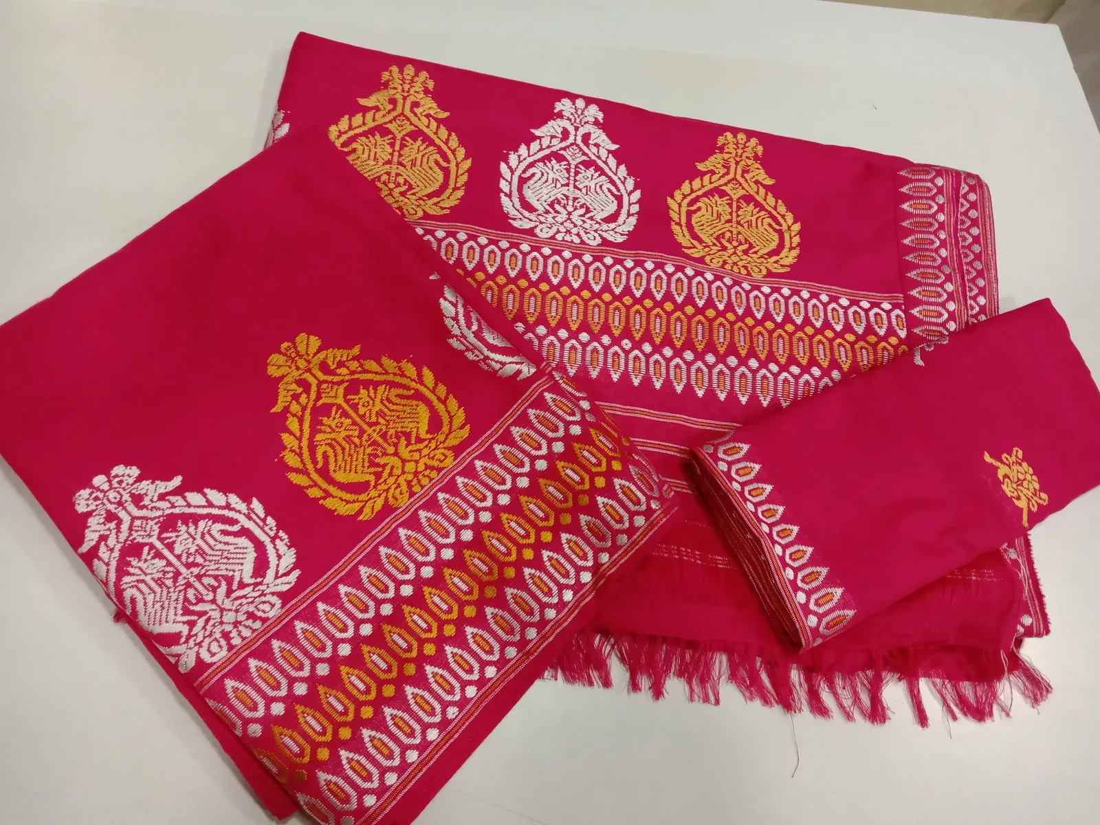 Folded bright pink mekhela sador set woven with gold and silver floral and peacock motifs along the borders
