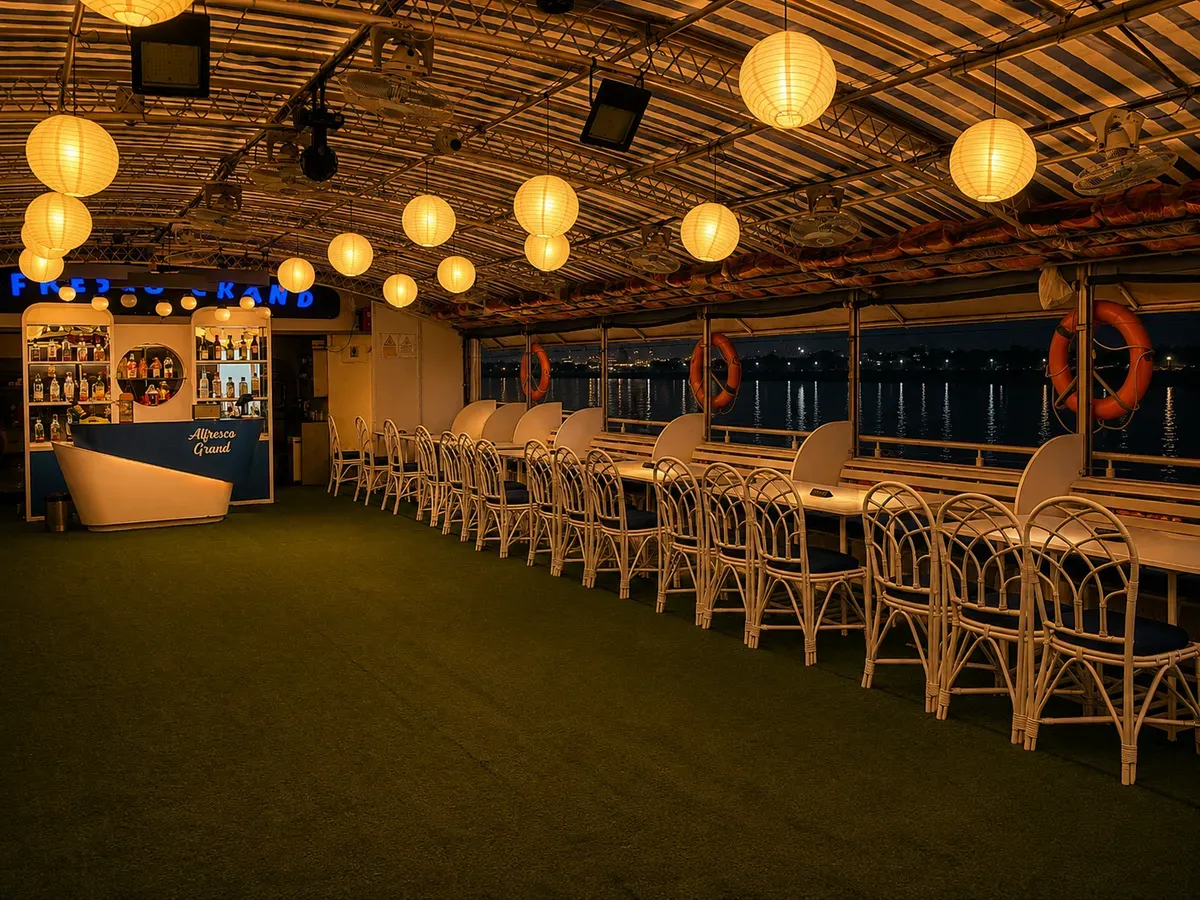Middle deck of Alfresco Grand at night — bar and cane seating under paper lanterns, the river lights beyond