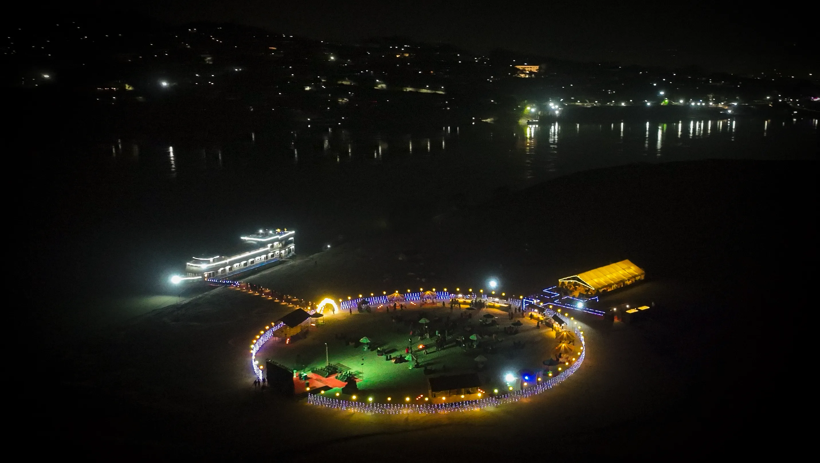 Night aerial of the lit river island event venue with the vessel docked alongside