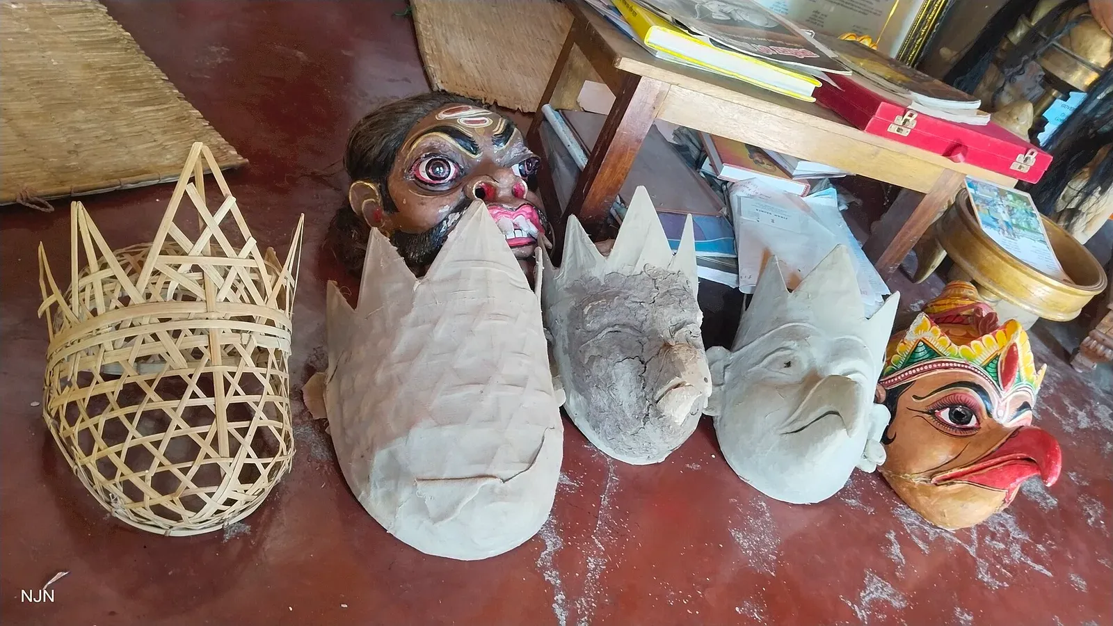 Bhaona masks in different stages at Samaguri Satra — a woven bamboo frame, clay-coated forms and finished painted faces of a bearded character and a bird-beaked Garuda