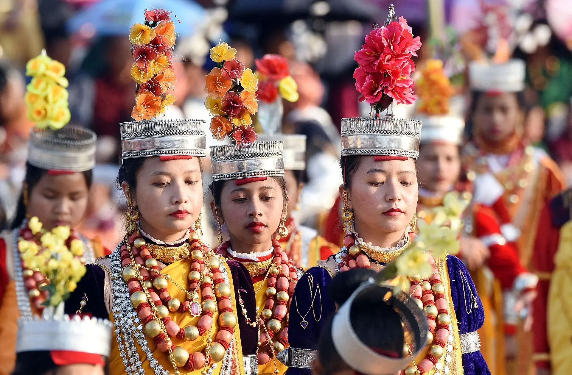 Young Khasi dancers at Shad Suk Mynsiem in silver crowns topped with tall flower sprays, layered coral and gold bead necklaces and silk, moving through a festival crowd